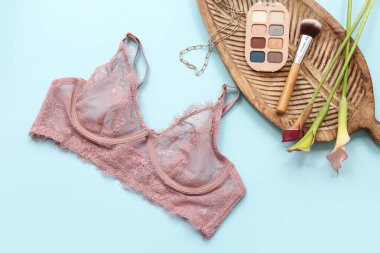Renk arkaplanında dantelli kadın sütyeni, çiçek ve kozmetik ürünleri olan kompozisyon