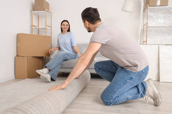 Young man with his wife rolling out carpet in room on moving day