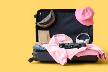 Sarı zemin üzerinde klasik daktilo, kitap ve giysiler bulunan bavulu aç