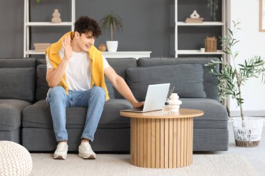 Genç adam evdeki kanepede video sohbeti yapıyor.