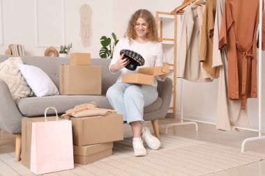 Evdeki kanepede yeni bereyle paket kutusunu açan genç bir kadın.