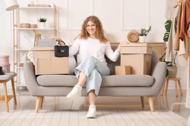 Paket kutularıyla evdeki kanepede oturan genç bir kadın.