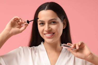 Pembe arka planda maskarası olan bornozlu güzel bir genç kadın.