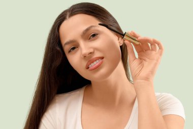 Açık yeşil arka planda rimel fırçası olan güzel bir genç kadın.