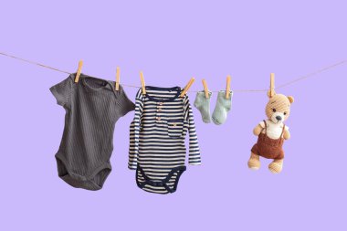Çorapları ve oyuncakları olan bebek kıyafetleri ipte leylak arka planda asılı.