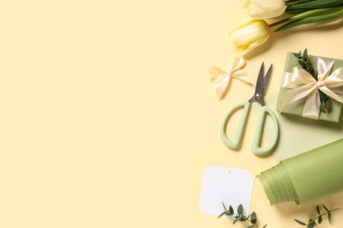 Laleli hediye kutusu, ambalaj kağıdı ve açık sarı arka planda makas. Uluslararası Kadınlar Günü