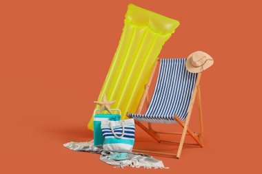 Şişme şiltesi, plaj soğutucusu ve turuncu arka planda yaz aksesuarları olan bir şezlong. Tatil kavramı