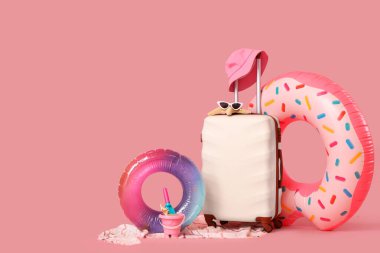 İçinde şişme yüzükler ve pembe arka planda plaj aksesuarları olan bavul. Tatil kavramı