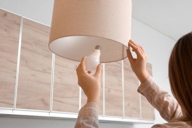 Evdeki şık asılı lambada ampulü değiştiren kadın, yakın plan.