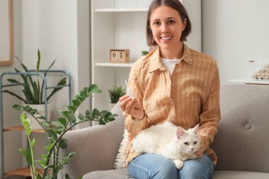 Kedili ve anti-parazit aplikatörlü genç bir kadın evdeki kanepede oturuyor.