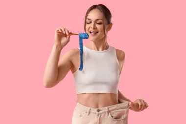 Pembe arka planda bol pantolonlu ve çatal yiyen genç bir kadın. Diyet kavramı