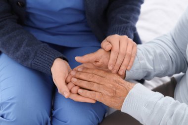 Bakıcı, yatak odasında el ele tutuşan yaşlı bir kadın, yakın çekim. Bakım kavramı