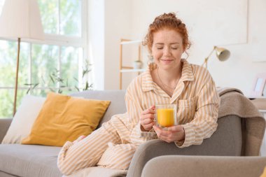 Evdeki kanepede pijamalı, zerdeçal içkili kızıl saçlı genç bir kadın.