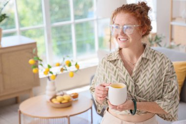 Evde zerdeçal içkisi olan genç kızıl saçlı kadın.