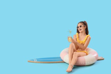 Kokteyl ve sörf tahtasıyla yüzme yüzüğünde mavi arka planda oturan tatlı kız.