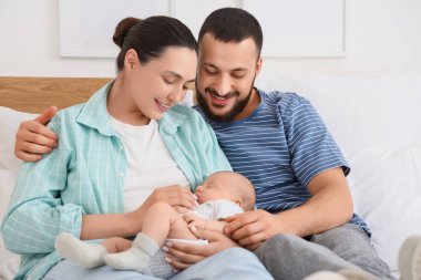 Mutlu ebeveynler ve küçük bebekleri yatak odasında sarılıyorlar.