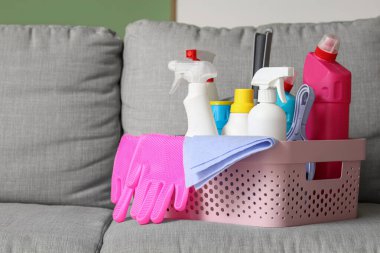 Gri kanepenin üzerinde temizlik malzemeleri olan sepet, yakın plan.