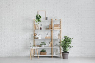 Raflar, masa ve bitkiler odanın içindeki beyaz tuğla duvarın yanında.