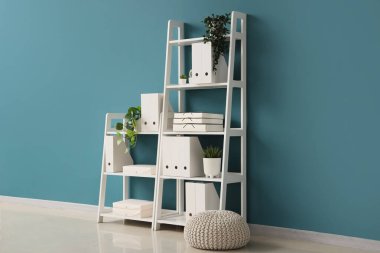 Pouf, ofis klasörlü raf ünitesi ve odanın içindeki mavi duvarın yanındaki ev bitkileri.