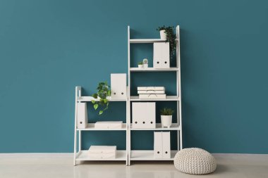 Pouf, ofis klasörlü raf ünitesi ve odanın içindeki mavi duvarın yanındaki ev bitkileri.