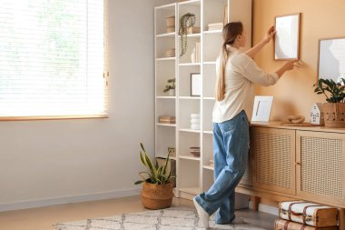 Evdeki duvara resim çerçevesi asan genç bir kadın.