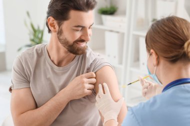 Genç adam klinikteki doktordan aşı alıyor.