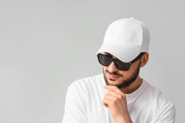 Gri arka planda güneş gözlüğü takan şık şapkalı yakışıklı bir genç.