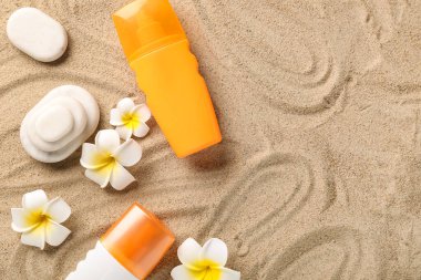 Güneş kremi şişeleriyle Plumeria çiçekleri ve kumdaki spa taşları