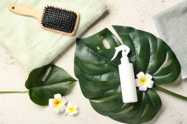 Saç spreyi, fırça, palmiye yaprakları ve açık arkaplanda tropikal çiçekler olan kompozisyon