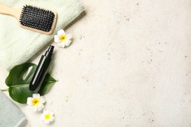 Saç spreyi, fırça, temiz havlu ve açık arkaplanda tropikal çiçekler olan kompozisyon