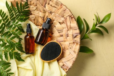 Arka planda saç spreyleri, fırçalar, kumaşlar ve eğreltiotu yapraklarıyla dolu bir hasır levha.