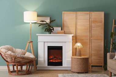 Katlanan perdeli oturma odası, parlayan lambalar, koltuk, hasır masa ve mavi duvarın yanındaki şömine dekoru.