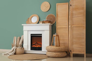 Oturma odasındaki turkuaz duvarın yanında katlanmış perdeli ve dekorlu şömine.