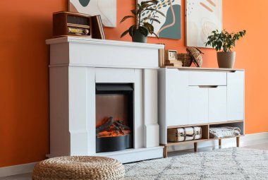 Oturma odasında turuncu duvarın yanında radyo, klozet ve dekor olan bir şömine.