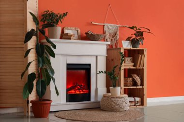 Katlanmış perdeli şömine, raf ünitesi ve oturma odasındaki turuncu duvarın yanındaki dekor.