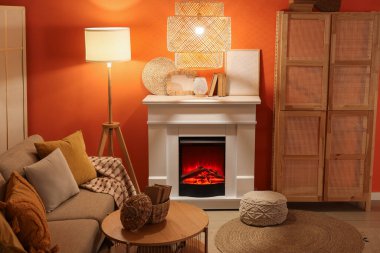 Oturma odasındaki kanepe, dolap ve turuncu duvarın yanında parlayan lambalar olan şömine.