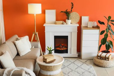 Kanepesi, tuvaleti ve turuncu duvarın yanında parlayan lambası olan bir şömine.