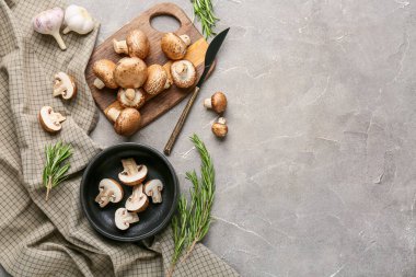 Kesme tahtası, peçete ve gri grunge arka planda çiğ şampiyon mantarları.