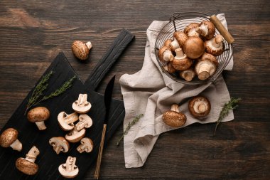 Tahta ve kevgir, kahverengi ahşap arka planda çiğ şampiyon mantarlarıyla kesiliyor.