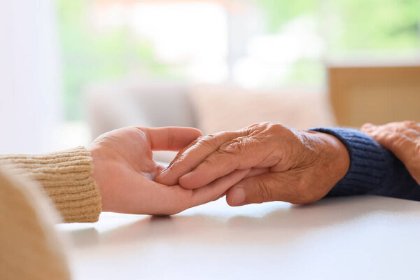 Woman holding grandmother's hand on table, closeup. Care concept
