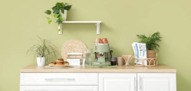 Modern kahve makinesi, fincanlar, gazete ve çörekler mutfaktaki masada.