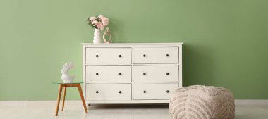 Çekmeceler, puf ve sehpa modern odada yeşil duvarın yanında.