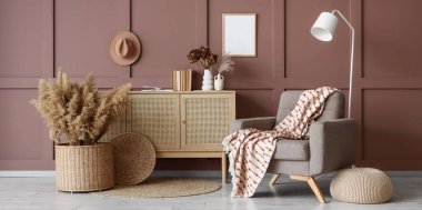 Rahat koltuk, ahşap tuvalet, puf ve zemin lambası oturma odasındaki kahverengi duvarın yanında.