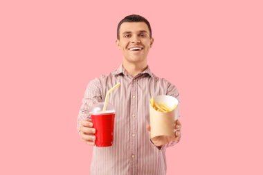 Young man with french fries and cola on pink background