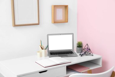 Pembe duvarın yanında dizüstü bilgisayarı ve kırtasiyesi olan güzel bir iş yeri.