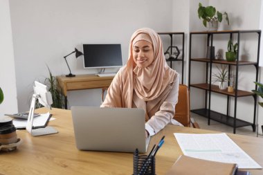 Masada dizüstü bilgisayarla çalışan Müslüman iş kadını.