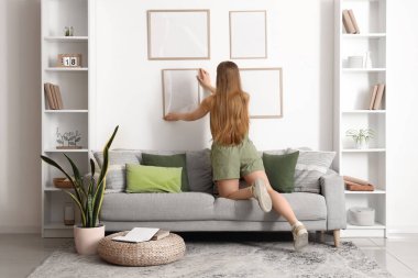 Oturma odasındaki duvara çerçeveyi asan genç bir kadın.