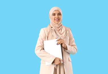 Mavi arka planda dizüstü bilgisayarı olan güzel bir Müslüman iş kadını.