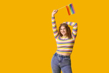 Sarı arka planda LGBT bayrağı olan mutlu genç bir kadın.