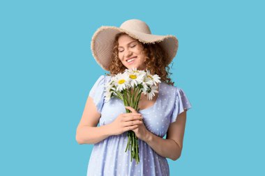 Mavi arka planda bir buket papatya çiçeğiyle mutlu genç bir kadın.